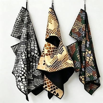 Eliteshine MH-C club slit golf towels in three colourways — black, tan, and green snake-print digital designs hanging from hooks on white wall